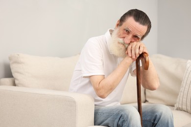 Photo of Senior man with walking cane on sofa indoors