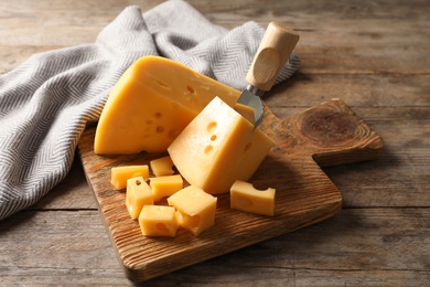 Photo of Serving board with delicious cheese on wooden table