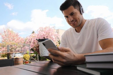 Happy man with smartphone and coffee listening to audiobook in outdoor cafe