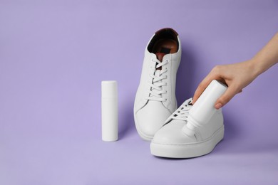 Woman cleaning stylish white sneakers on violet background, closeup. Space for text