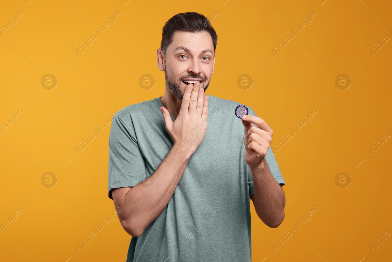 Photo of Confused man holding condom on orange background