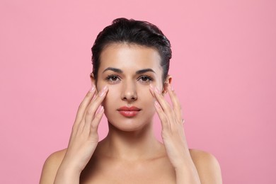 Photo of Woman applying cream under eyes on pink background. Skin care