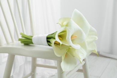 Photo of Beautiful calla lily flowers tied with ribbon on white chair indoors