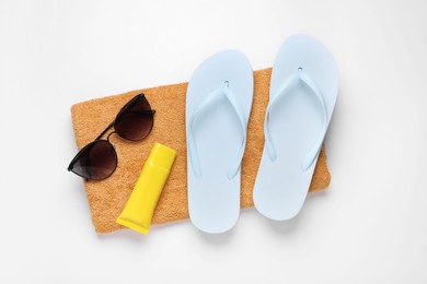 Photo of Flip flops, sunscreen, stylish sunglasses and soft towel on white background, top view. Beach accessories