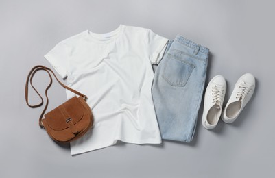 Stylish t-shirt, jeans and sneakers on light grey background, flat lay