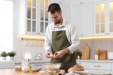 Making bread. Man putting raw egg into dough at wooden table in kitchen