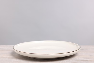 Photo of Empty ceramic plate on wooden table against light background, space for text