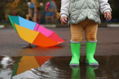 Photo of Little girl wearing light green rubber boots standing in puddle outdoors, closeup. Space for text