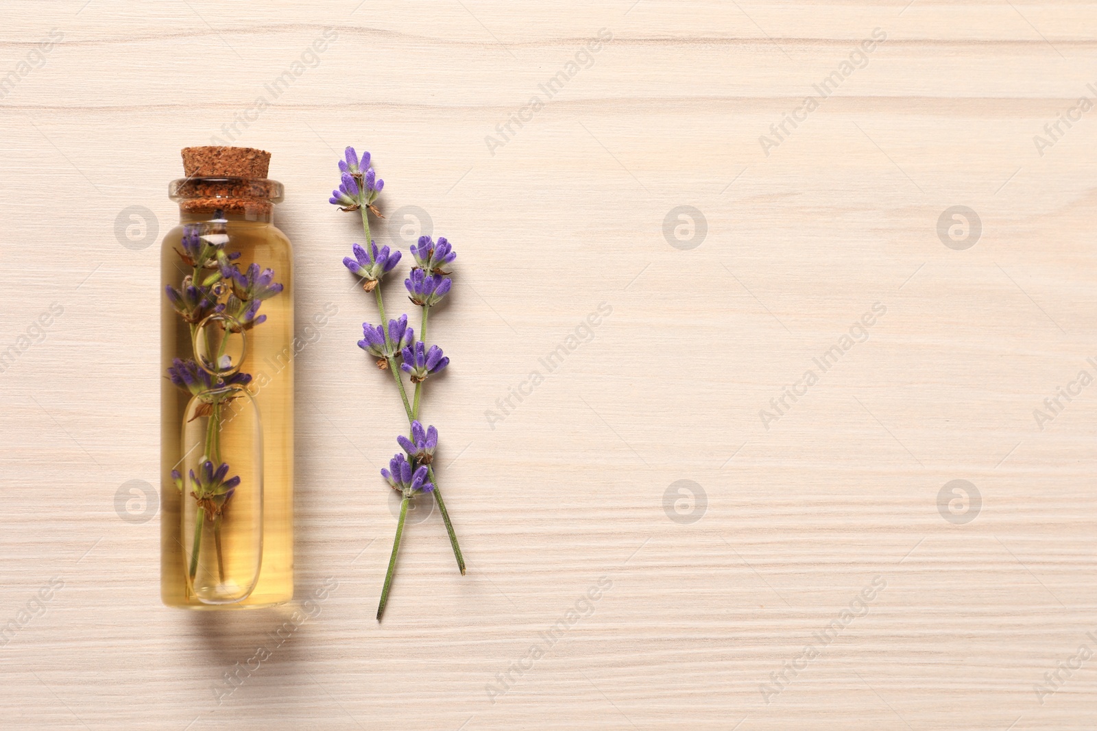 Photo of Bottle of essential oil and lavender flowers on white wooden table, flat lay. Space for text