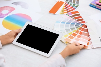 Photo of Woman with tablet and paint color palette samples at table, closeup