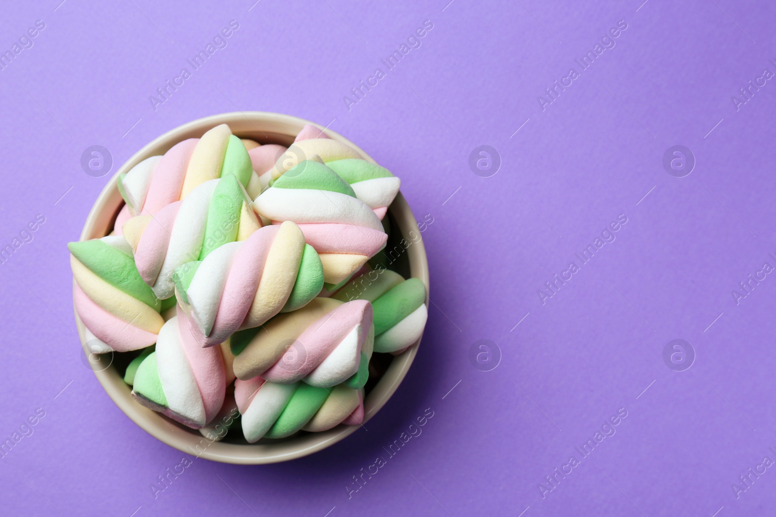 Photo of Delicious colorful marshmallows in bowl on violet background, top view. Space for text