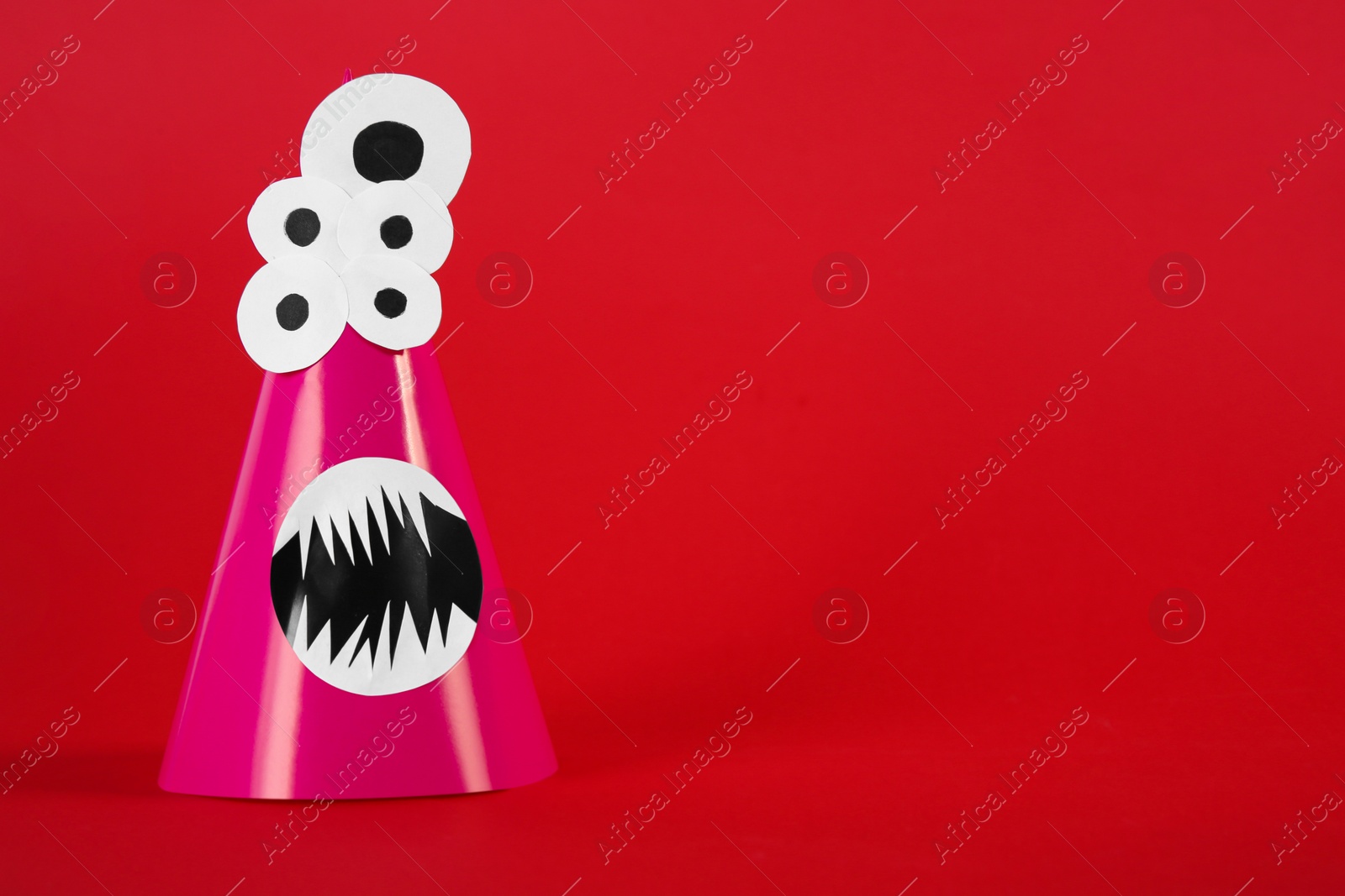 Photo of Funny pink monster on red background, space for text. Halloween decoration