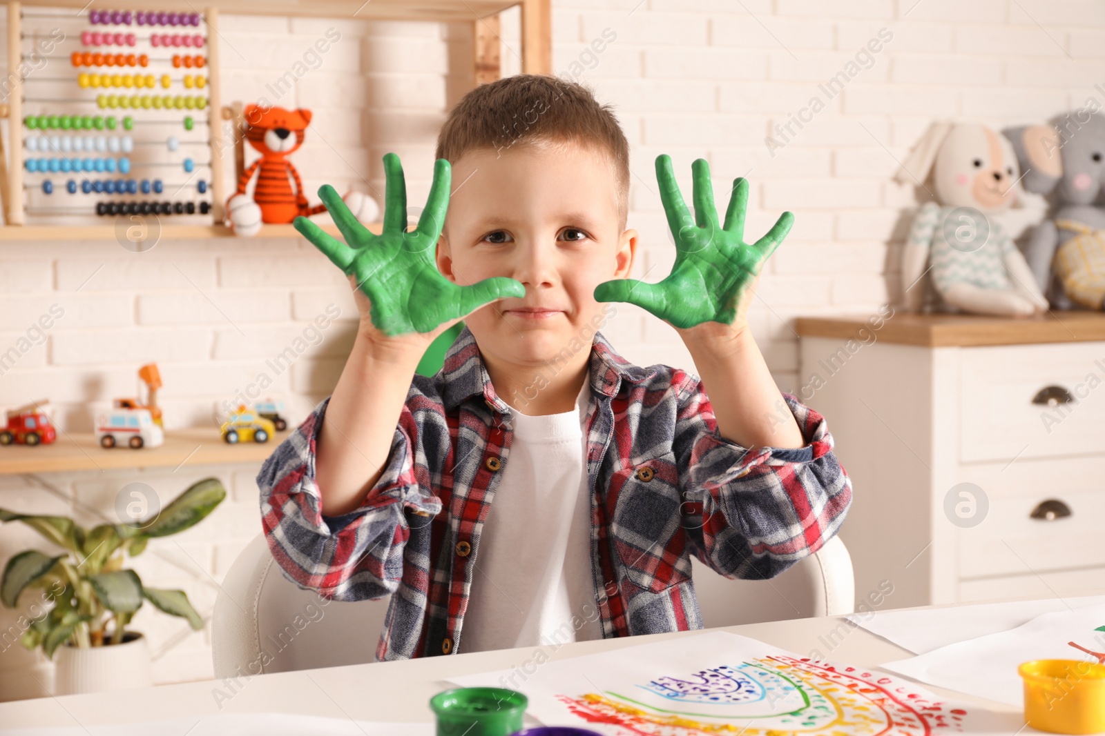 Photo of Little boy showing painted palms at white table indoors
