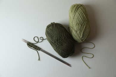 Photo of Soft green yarns, knitting and metal needles on light background, flat lay