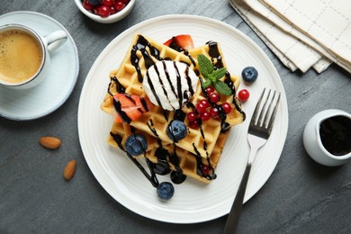 Delicious Belgian waffles with ice cream, berries and chocolate sauce served on grey textured table, flat lay