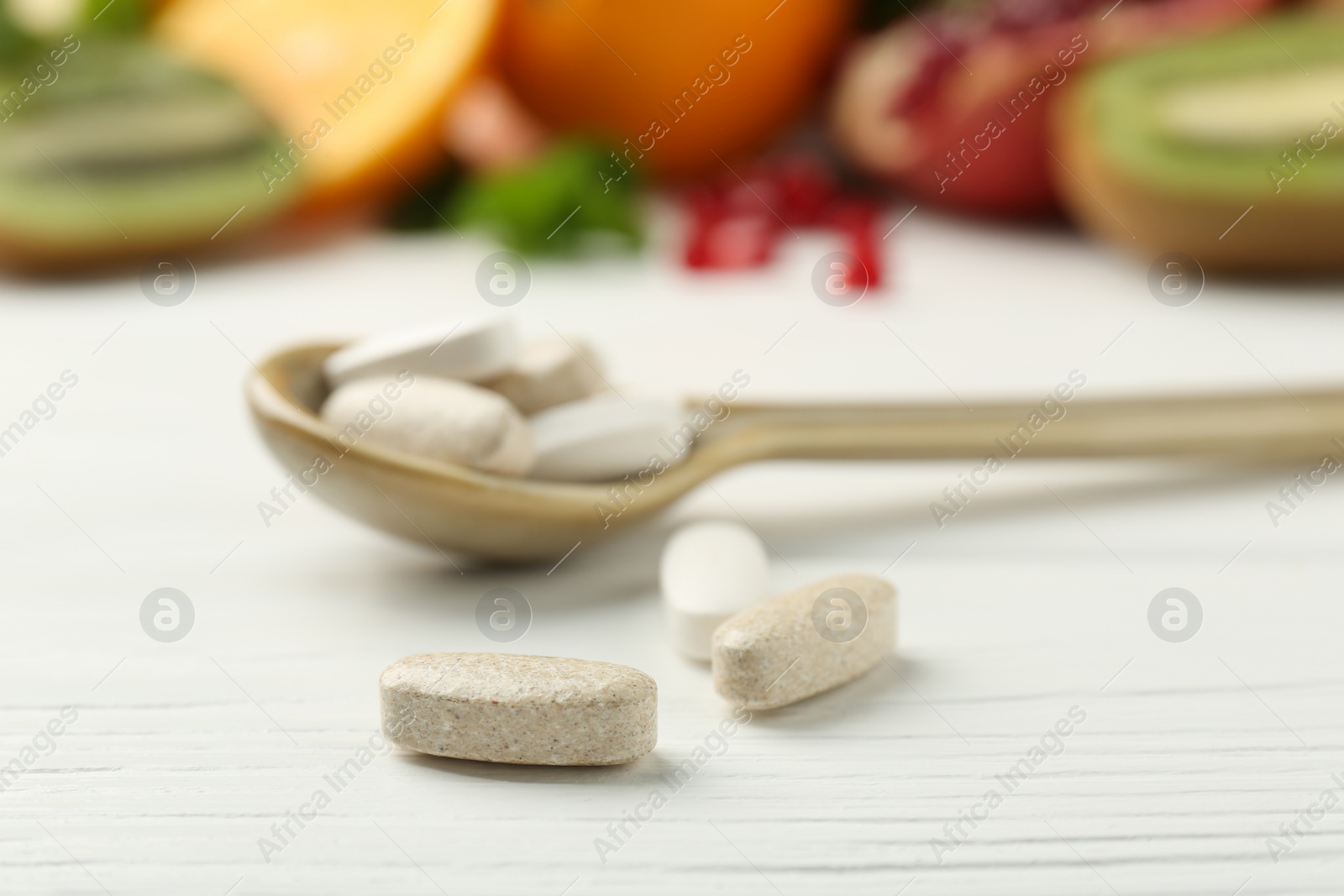 Photo of Different vitamin pills in spoon on white wooden table