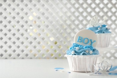 Delicious cupcakes with light blue cream and toppers on white table, space for text. Baby shower party