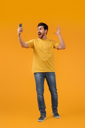 Photo of Emotional man taking selfie with smartphone on yellow background