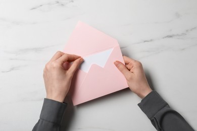 Photo of Woman taking card out of letter envelope at marble table, top view