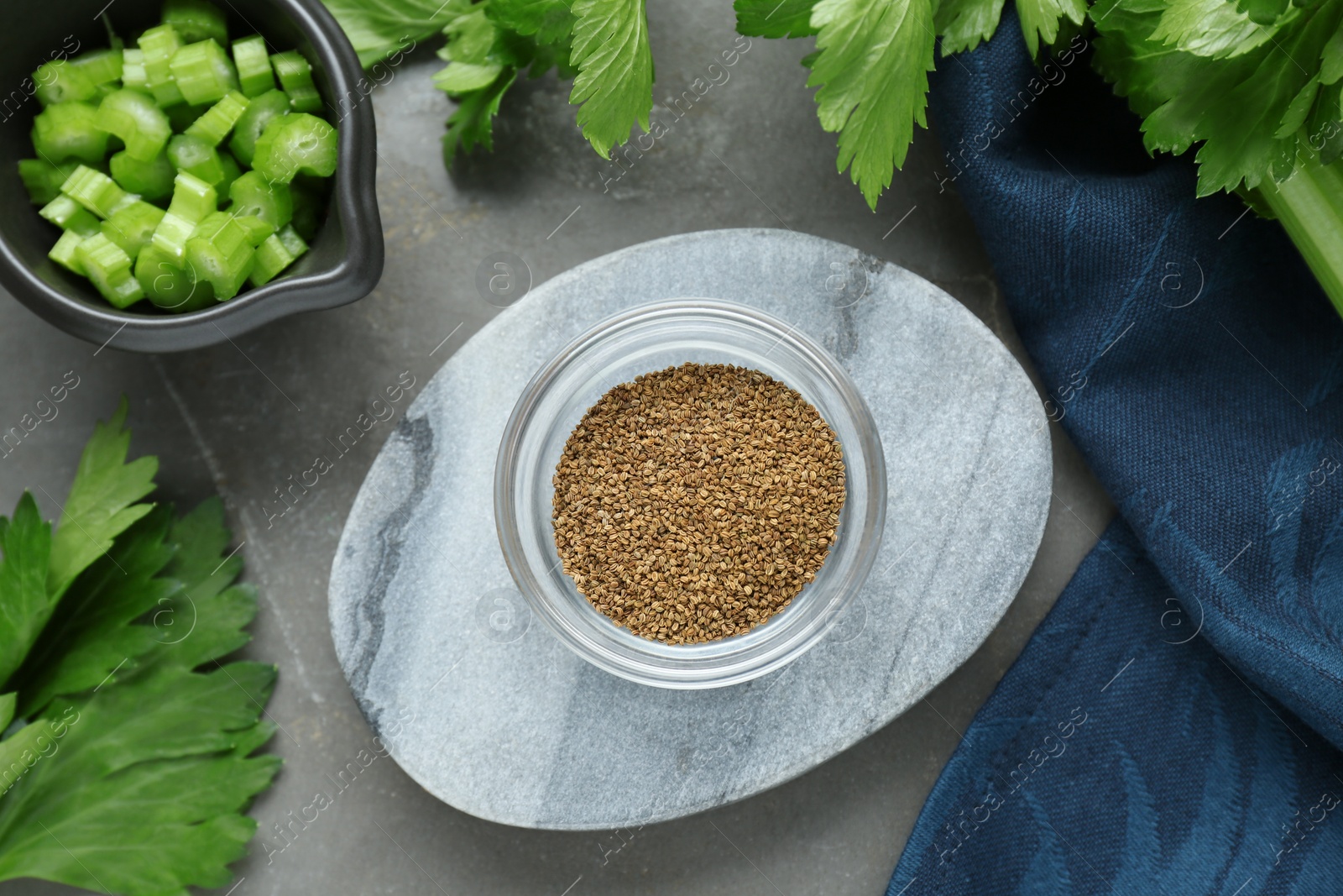 Photo of Bowl of celery seeds and fresh plant on grey table, flat lay