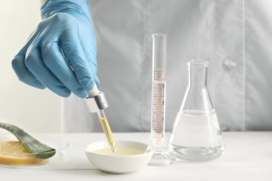 Scientist developing cosmetic oil at white table, closeup