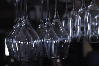 Photo of Set of empty clean glasses hanging upside down on dark background