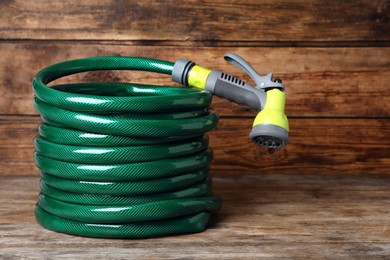 Green garden hose with spray gun on wooden table