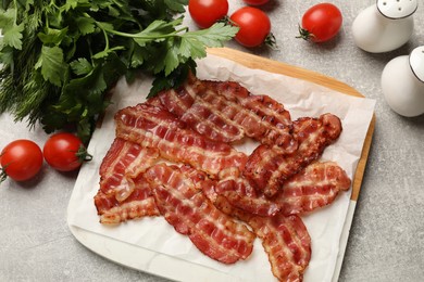 Photo of Fried bacon slices, tomato, parsley and spices on grey textured table, flat lay