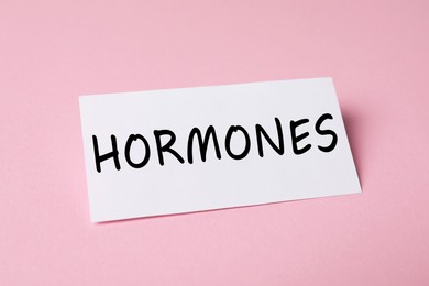 Photo of Sheet of paper with word Hormones on pink background