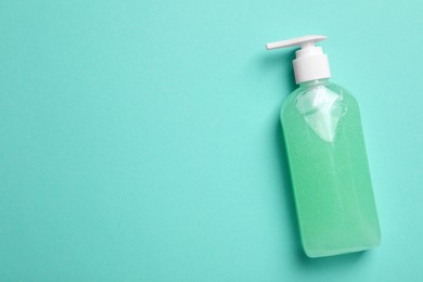 Photo of Bottle of face cleansing product on turquoise background, top view. Space for text