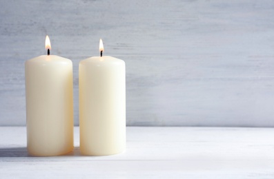 Photo of Beautiful burning wax candles on table against light background