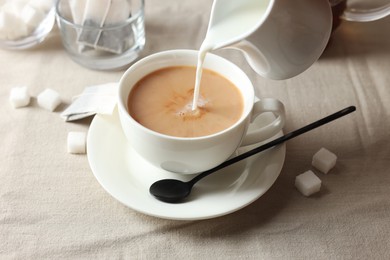 Photo of Pouring milk into cup with tea on light table, closeup