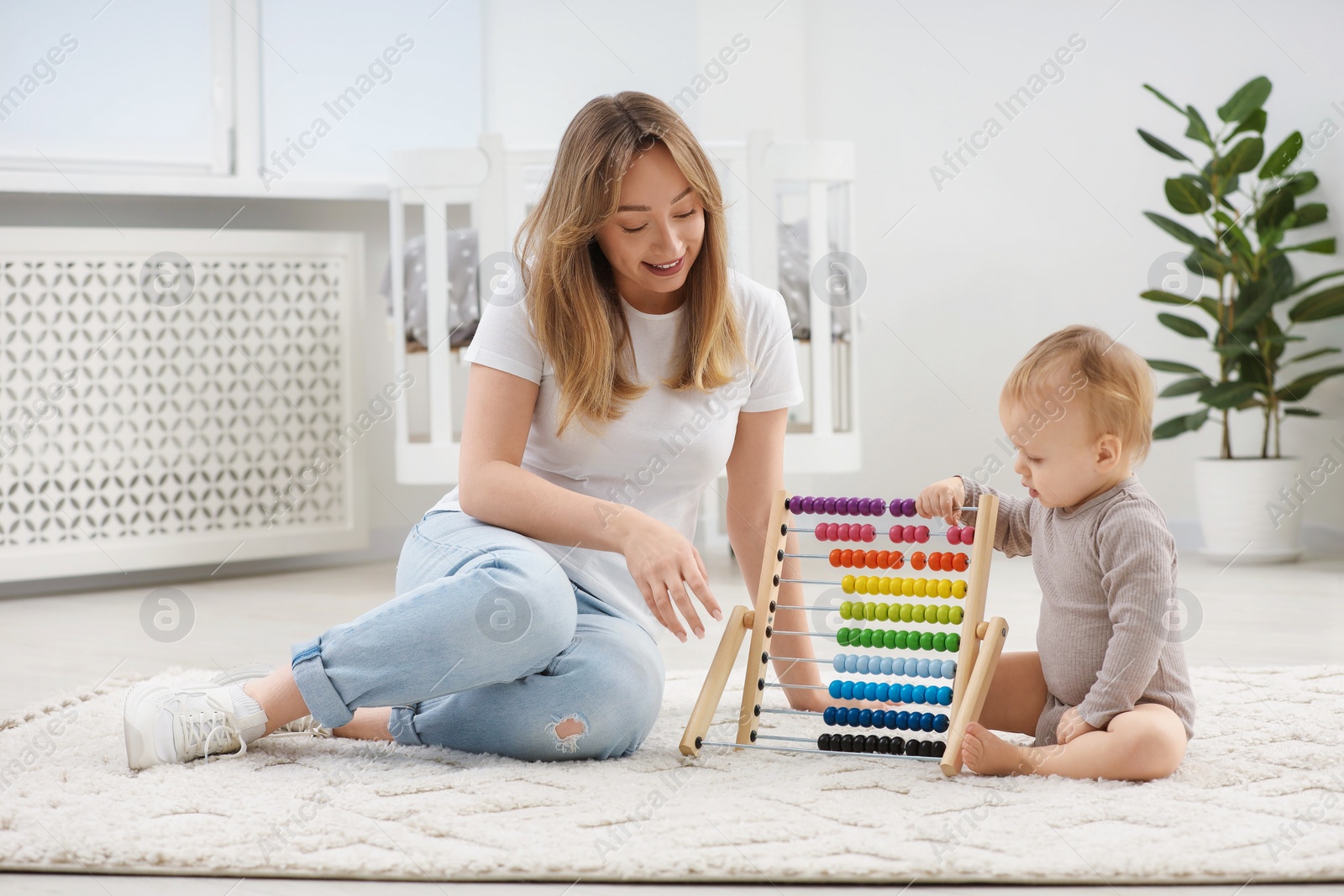 Photo of Children toys. Happy mother and her little son playing with wooden abacus on rug at home