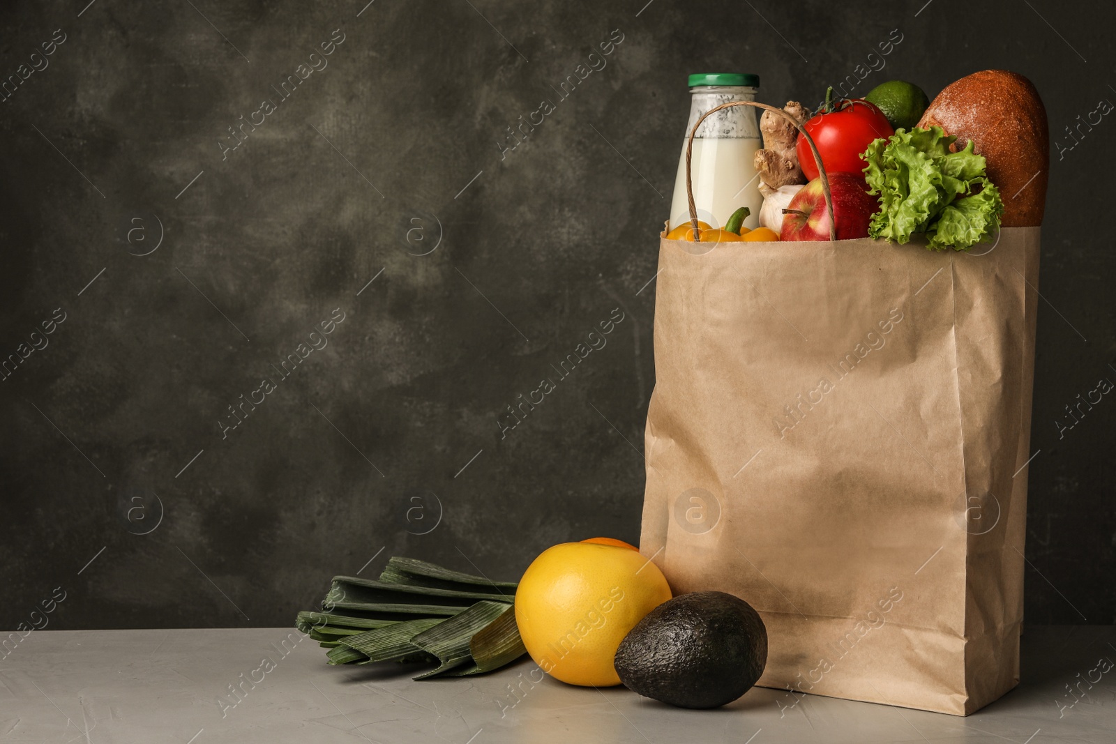 Photo of Paper bag with groceries on grey table against dark background. Space for text