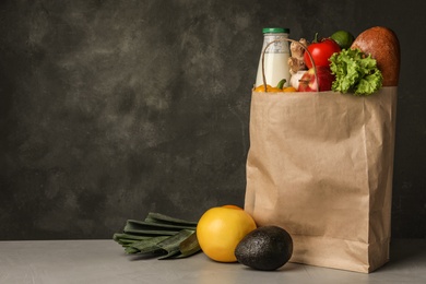 Paper bag with groceries on grey table against dark background. Space for text