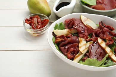 Photo of Delicious bresaola salad with sun-dried tomatoes, pear and balsamic vinegar served on white wooden table, closeup. Space for text