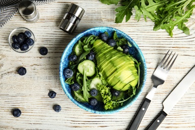 Photo of Delicious avocado salad with blueberries in bowl on white wooden table, flat lay