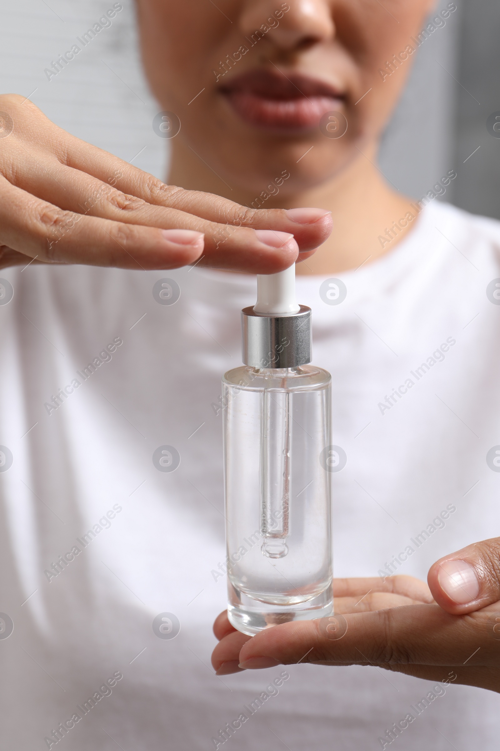 Photo of Woman with bottle of cosmetic serum on blurred background, closeup