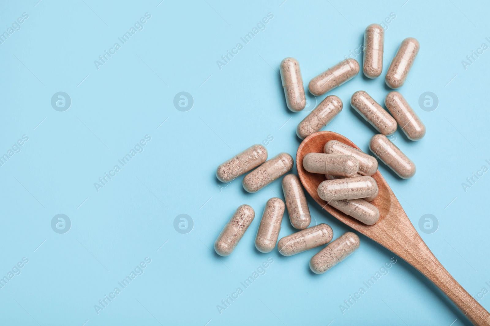 Photo of Many gelatin capsules and spoon on light blue background, flat lay. Space for text