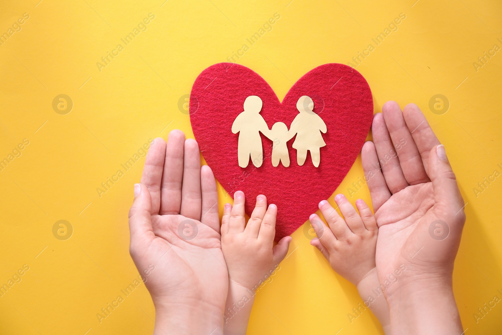 Photo of Young woman and child protecting red heart with paper silhouette of people on color background, top view