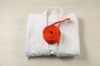 Photo of Orange karate belt and white kimono on wooden background, top view