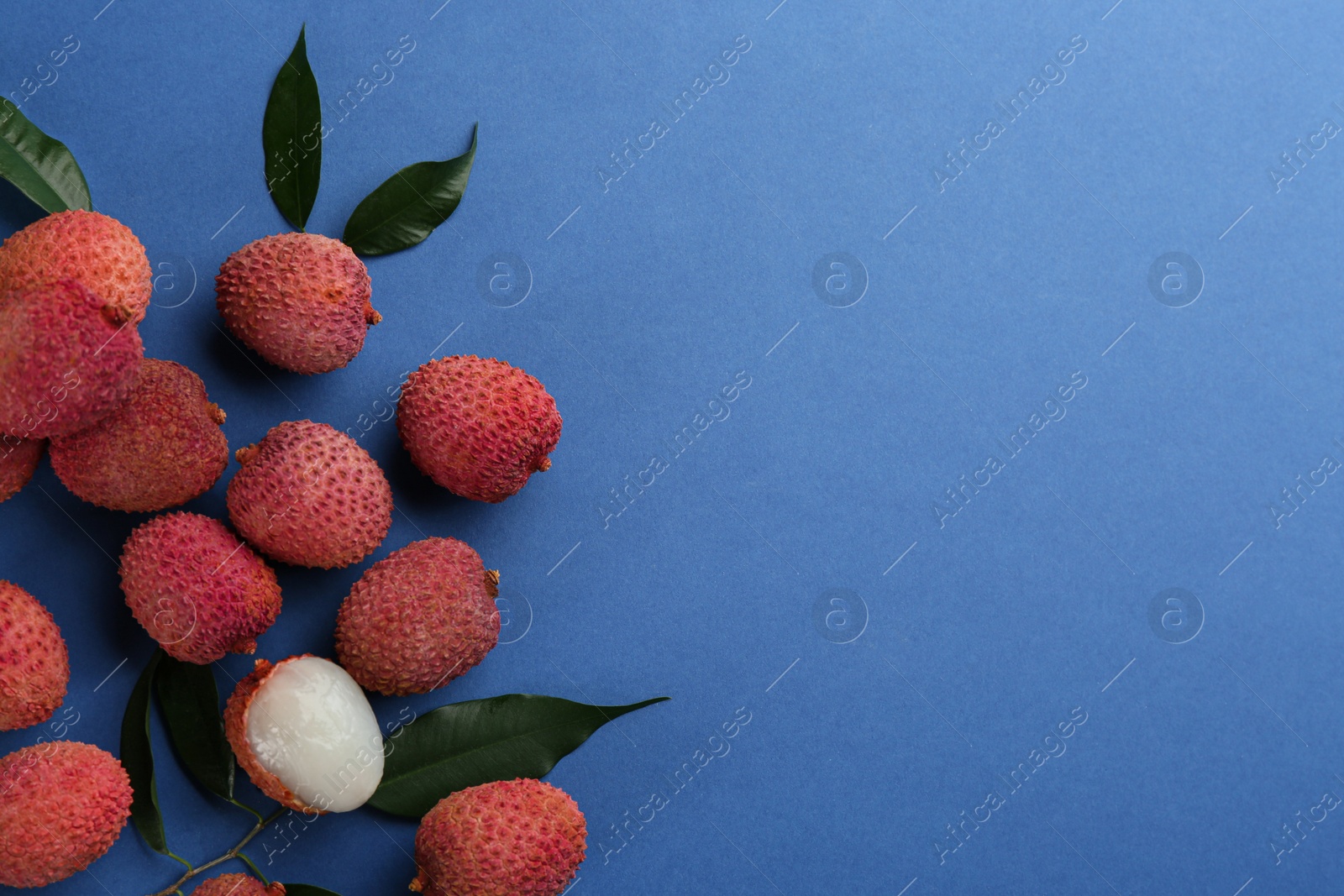 Photo of Fresh ripe lychees with leaves on blue background, flat lay. Space for text