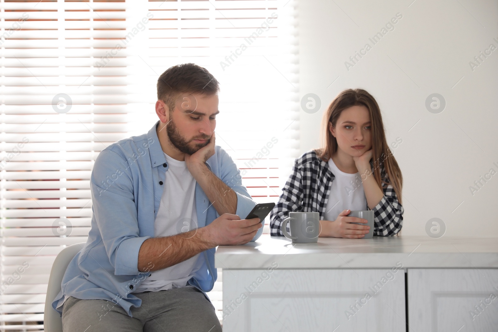 Photo of Young man preferring smartphone over his girlfriend at home. Relationship problems