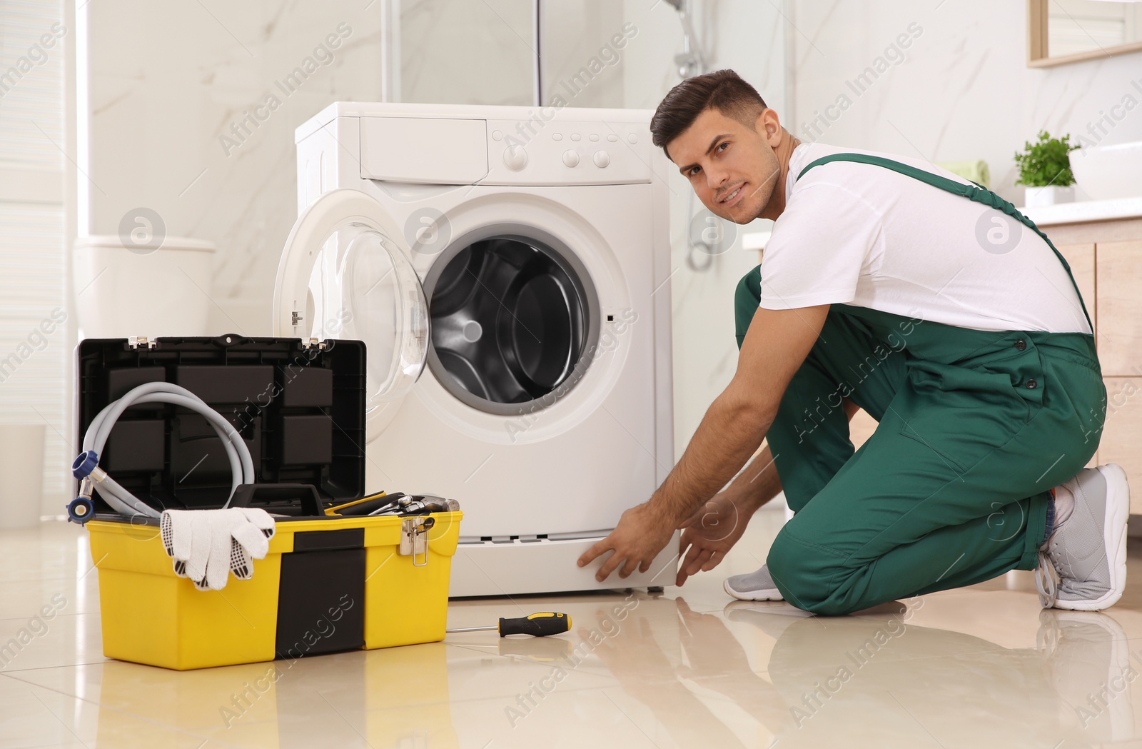Photo of Professional plumber repairing washing machine in bathroom