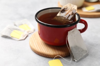 Tea bags and cup of hot beverage on light table, closeup