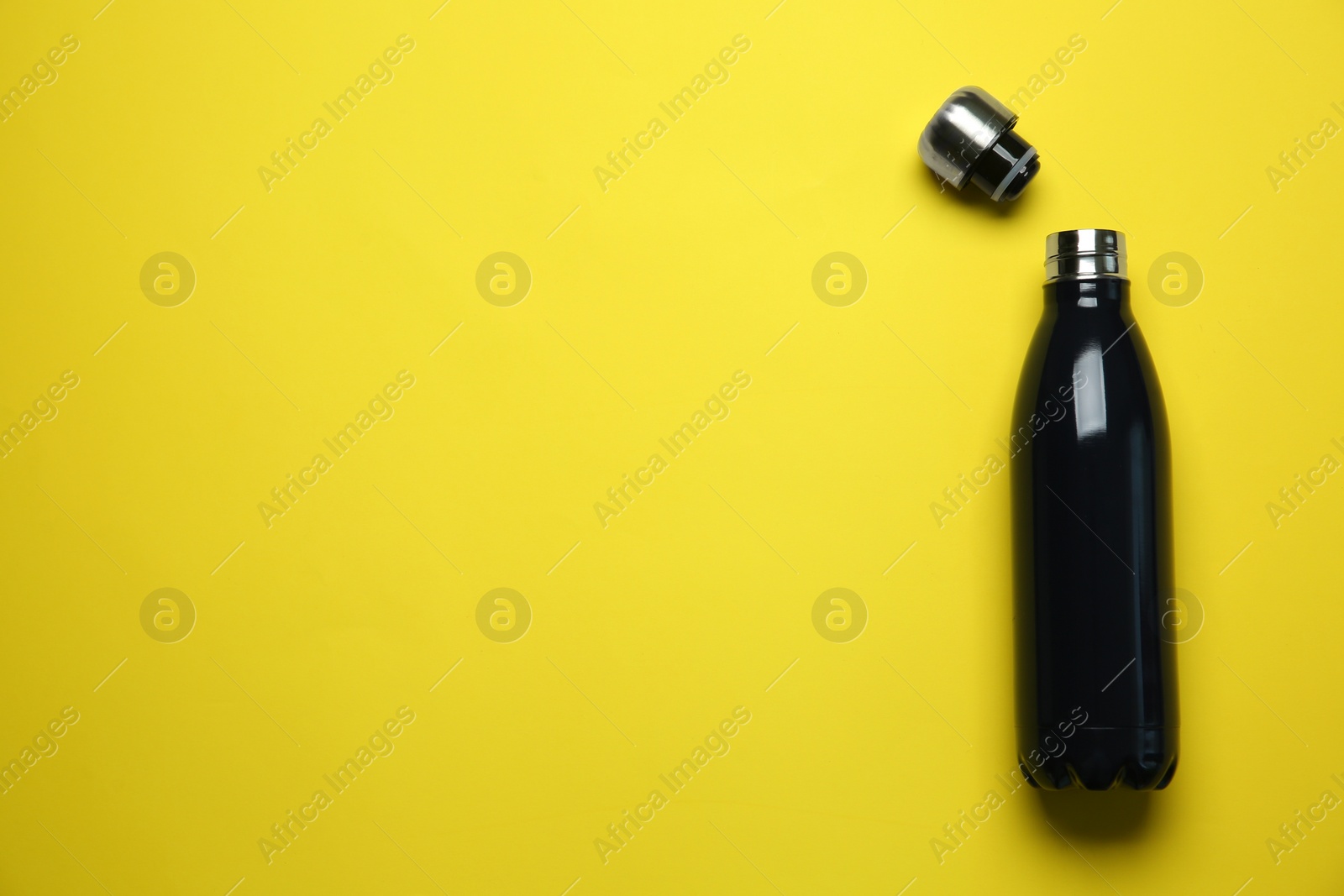 Photo of Black thermo bottle and cap on yellow background, flat lay. Space for text