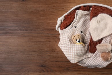 Laundry basket with baby clothes and crochet toy on wooden table, top view. Space for text