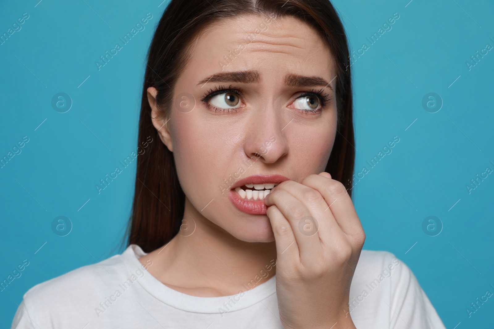 Photo of Young woman biting her nails on light blue background