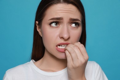 Young woman biting her nails on light blue background