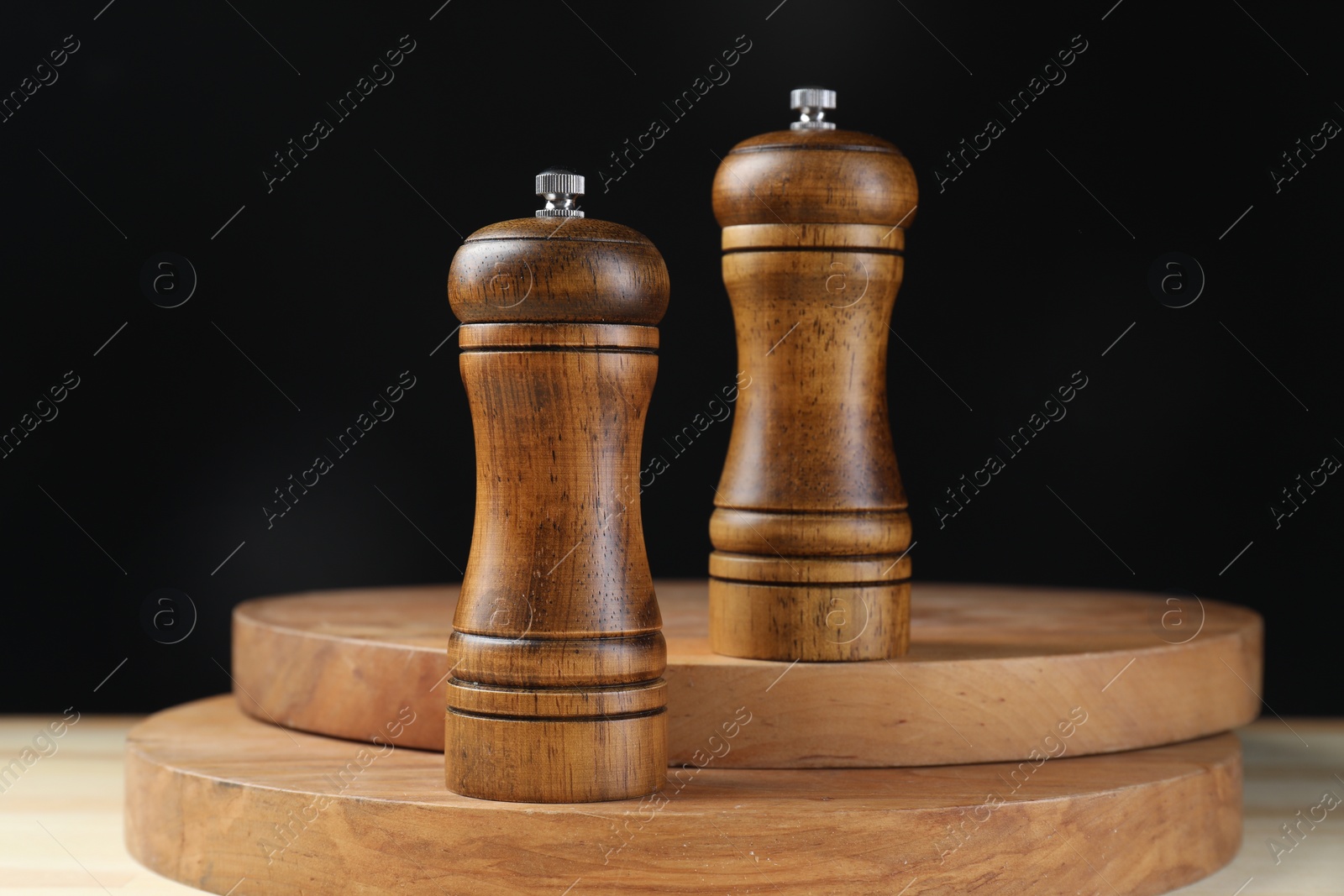 Photo of Salt and pepper shakers on wooden table against black background, closeup
